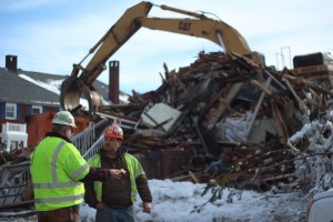ran Janaszek (left)  from Kebort Construction talks with a coworker as rubble from the demolished apartment complex is moved to a dumpster on Jan. 30, 2014. The blaze left at least nine families without a home. The demolition began at approximately 10 a.m. and ended at 2 p.m.  Spectators gathered throughout the process, many taking photos and videos. CAITIE McMEKIN/THE CAMPUS