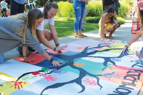 Rhiannon King, 20, Mary Allen, 22, and Marisol Santa Cruz, 20, make hand prints on a banner during the Climate Strike on Friday, Sept. 20, 2019, outside the Henderson Campus Center.