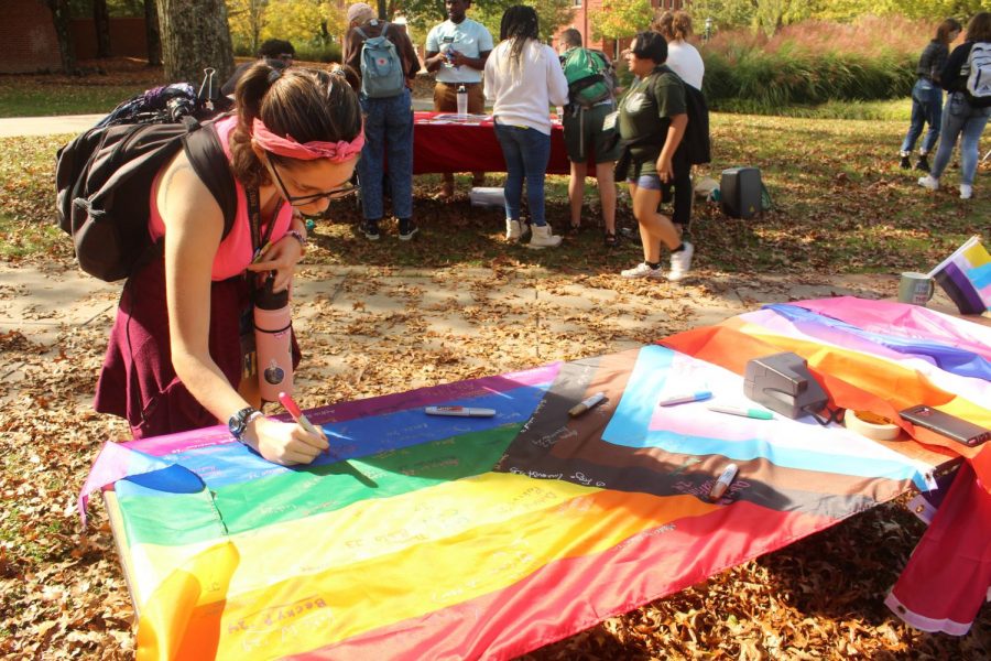 Furbish signs a “Progress” Pride flag as face-painting continues in the background. There are several variations to the traditional rainbow Pride flag that have been developed, including the six color (red, orange, yellow, green, blue, and purple), the Philadelphia flag, which adds black and brown to the six colors, and the “Progress” flag, inspired by the flag of South Africa.
