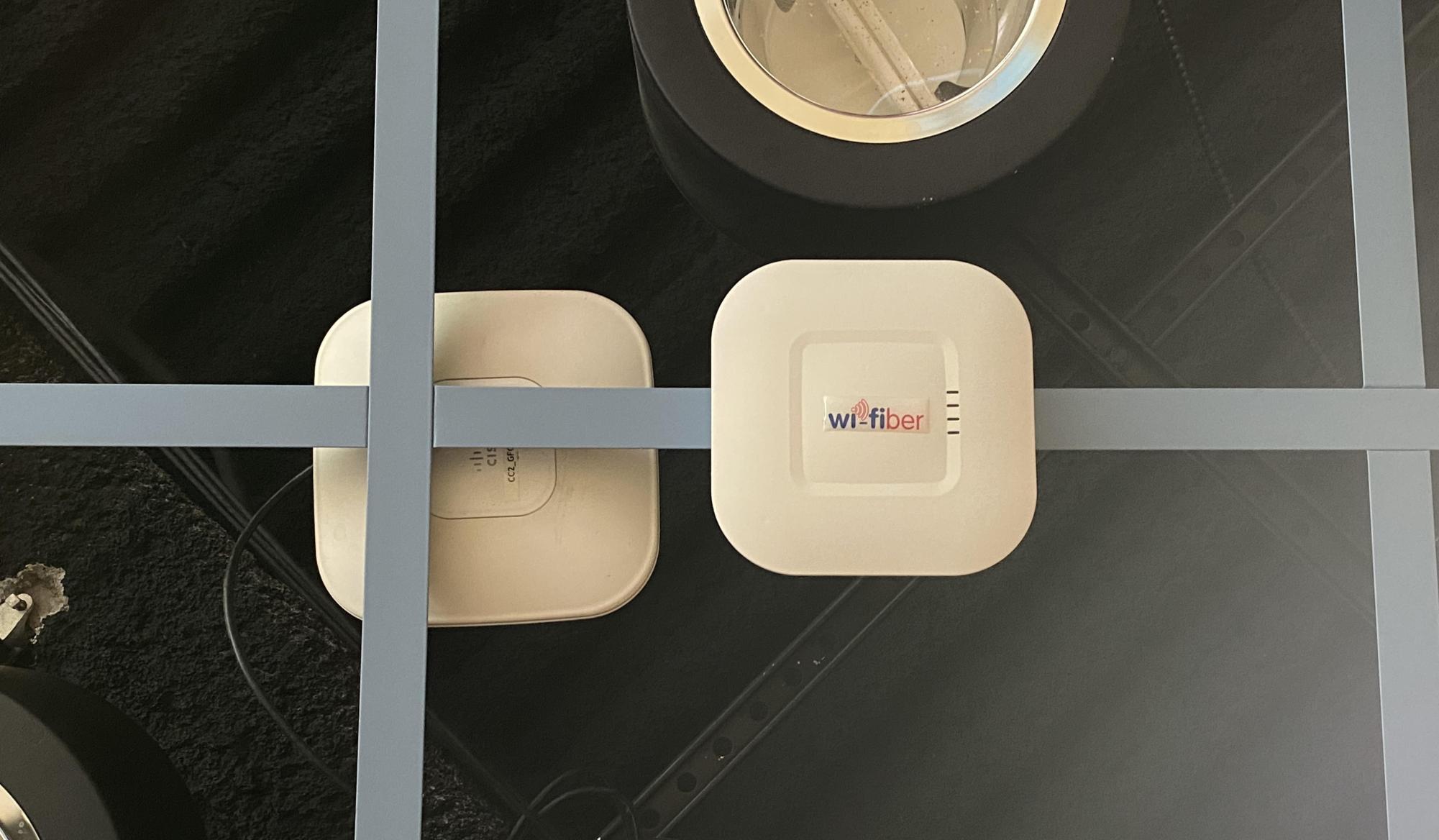 A Wi-Fiber access point in Grounds for Change is mounted to the ceiling, but not connected to the network. An older access point sporting an array of wires is mounted directly next to the Wi-Fiber access point.