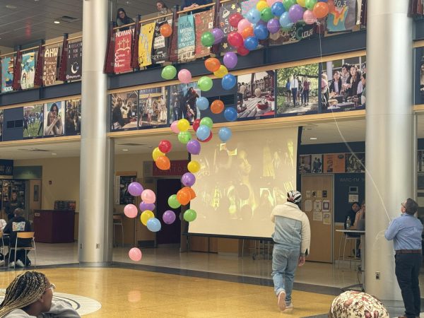 Thion Lee, ’24, turns away from the crowd after announcing that the headliner for the 2024 Springfest concert will be Flo Milli. Dean for Student Life Trae Yeckley (right) releases balloons in celebration of the announcement in the lobby of the Henderson Campus Center on Thursday, March 21.