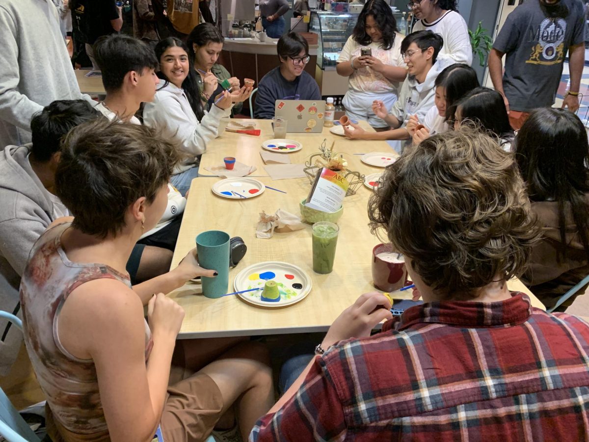 Attendees gather around the table painting their pots while sipping on coffee.